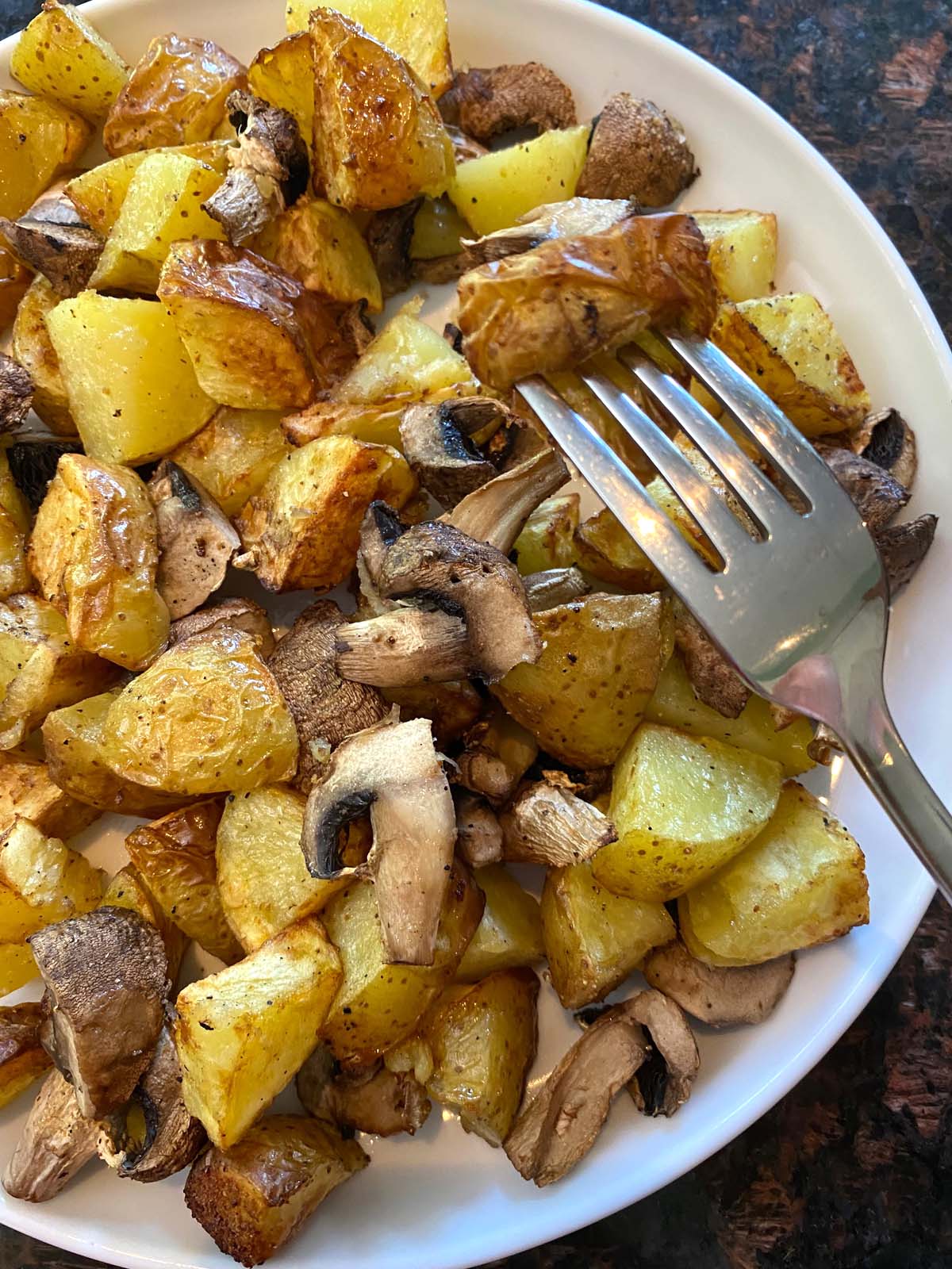 Cooked potatoes and mushrooms on a white plate.