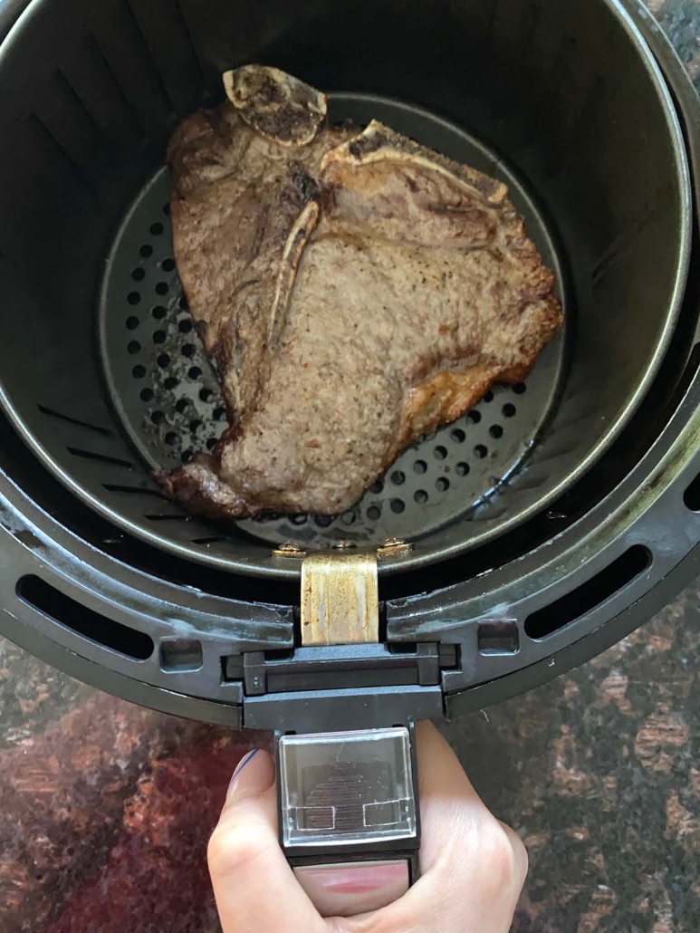 hand holding air fryer basket with steak inside