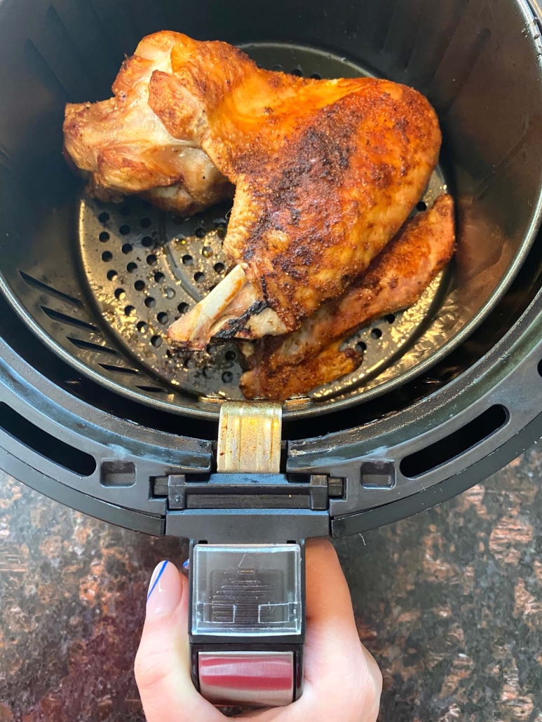 hand pulling air fryer open with turkey wing inside