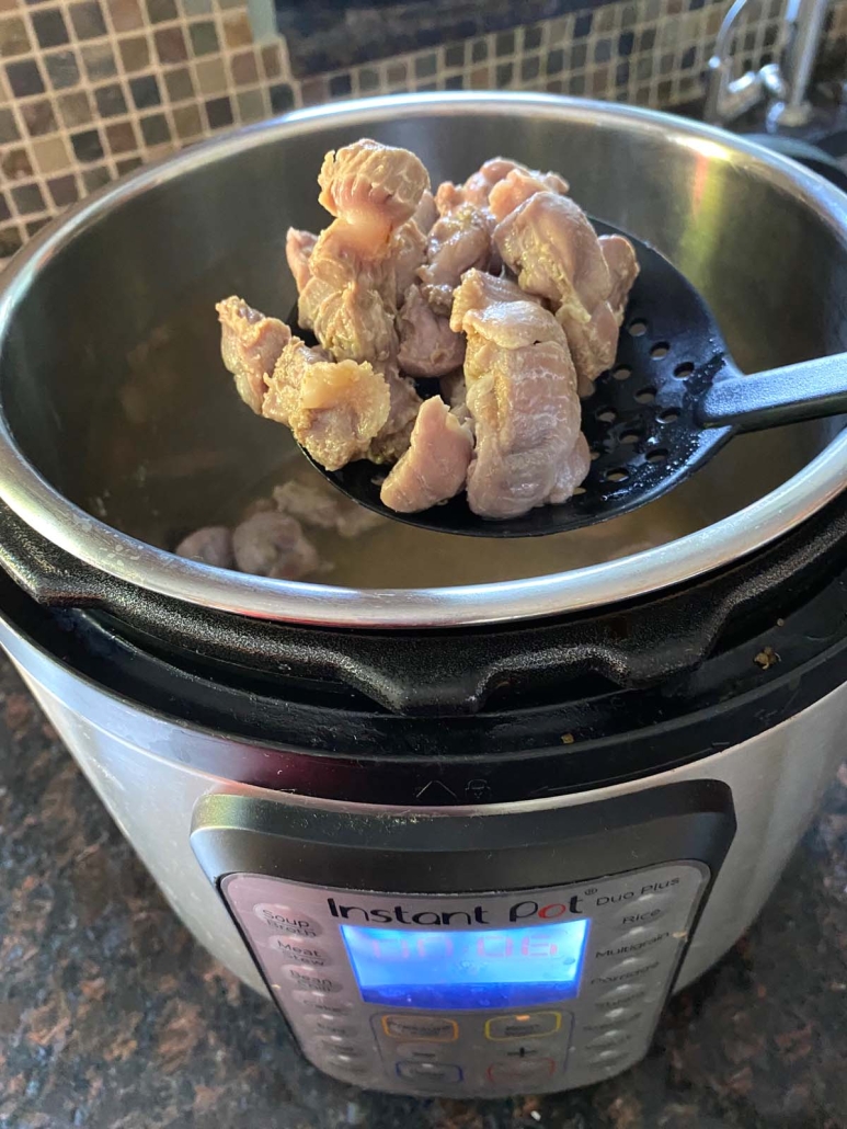slotted spoon scooping seasoned and cooked chicken gizzards out of instant pot