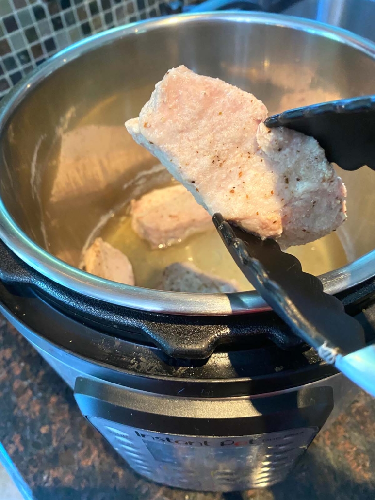 tongs holding pork ribs above instant pot