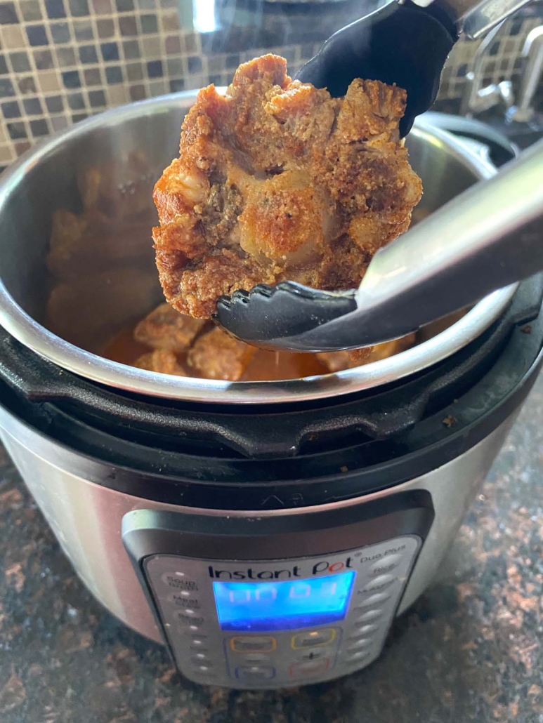 instant pot opened to show cooked oxtails in tongs