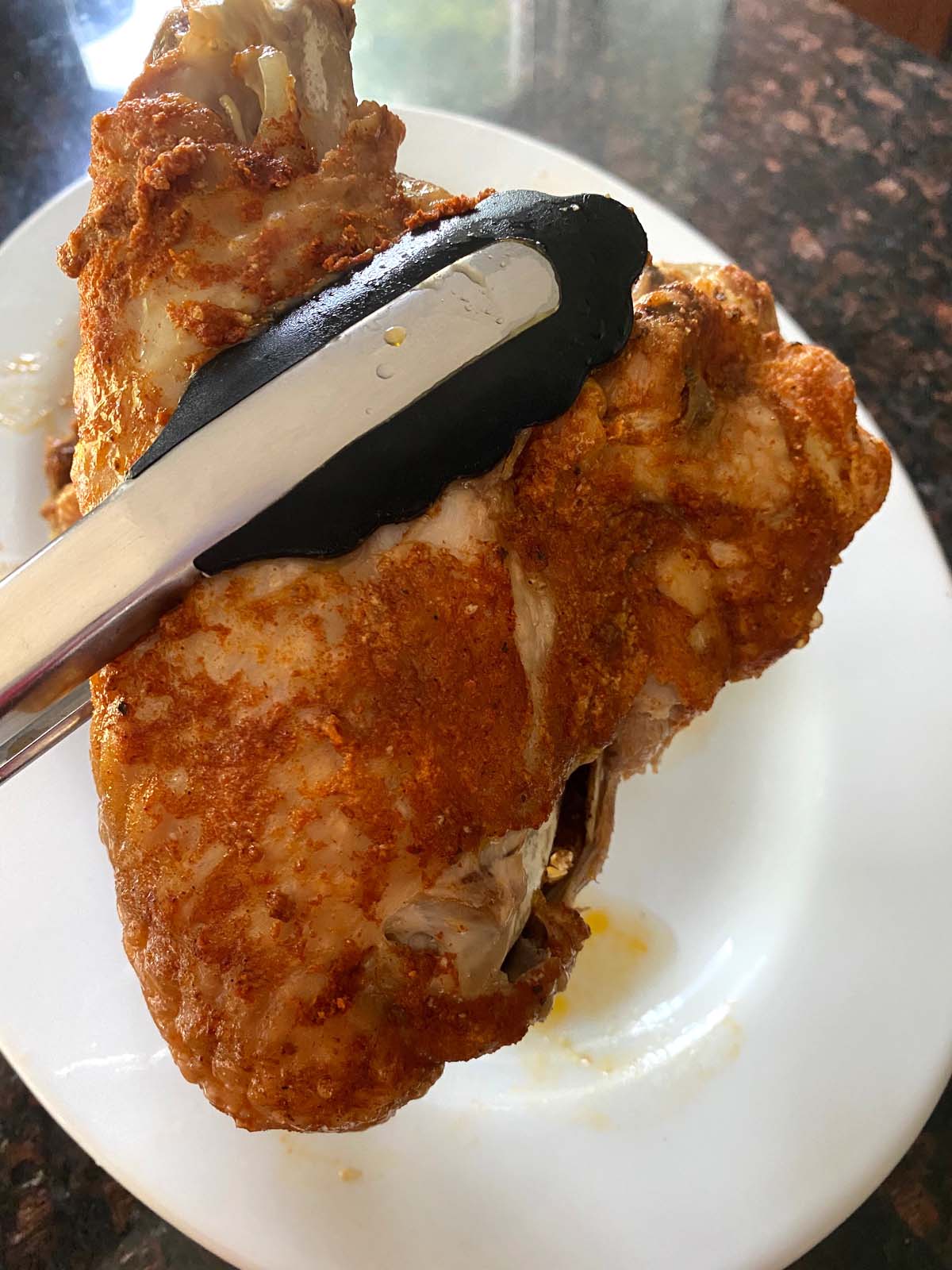 tongs holding a cooked and seasoned turkey wing