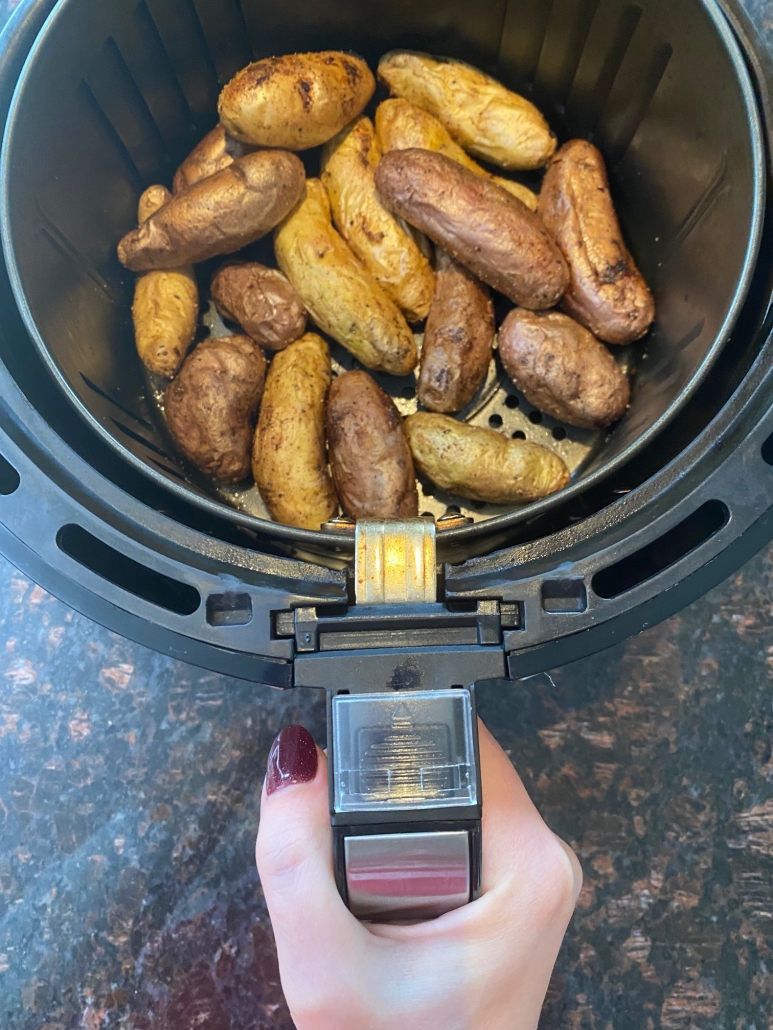 hand holding air fryer basket with fingerling potatoes