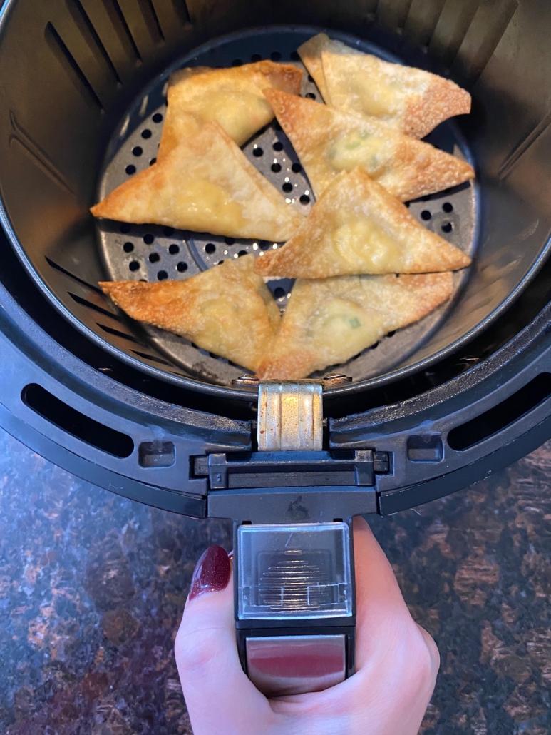hand holding air fryer basket with crab rangoon