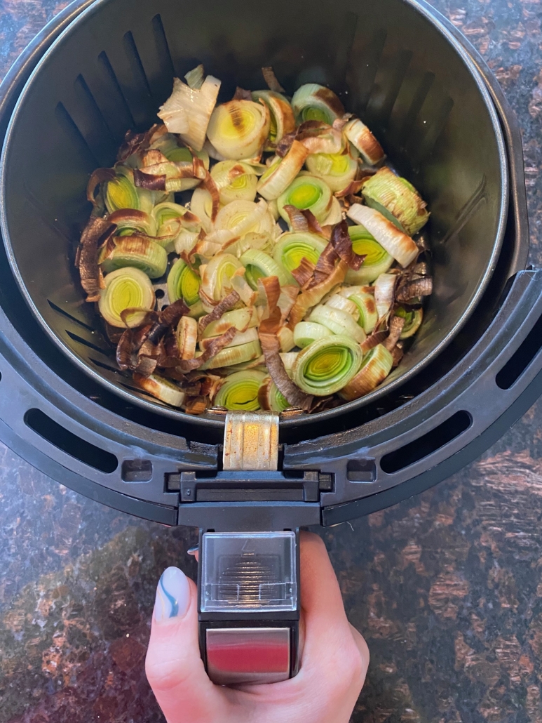 hand holding air fryer basket contained slices of leeks
