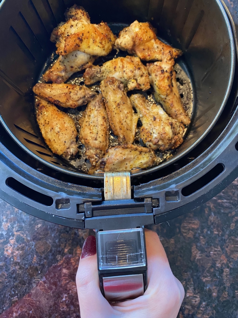 hand holding air fryer basket with lemon pepper chicken wings