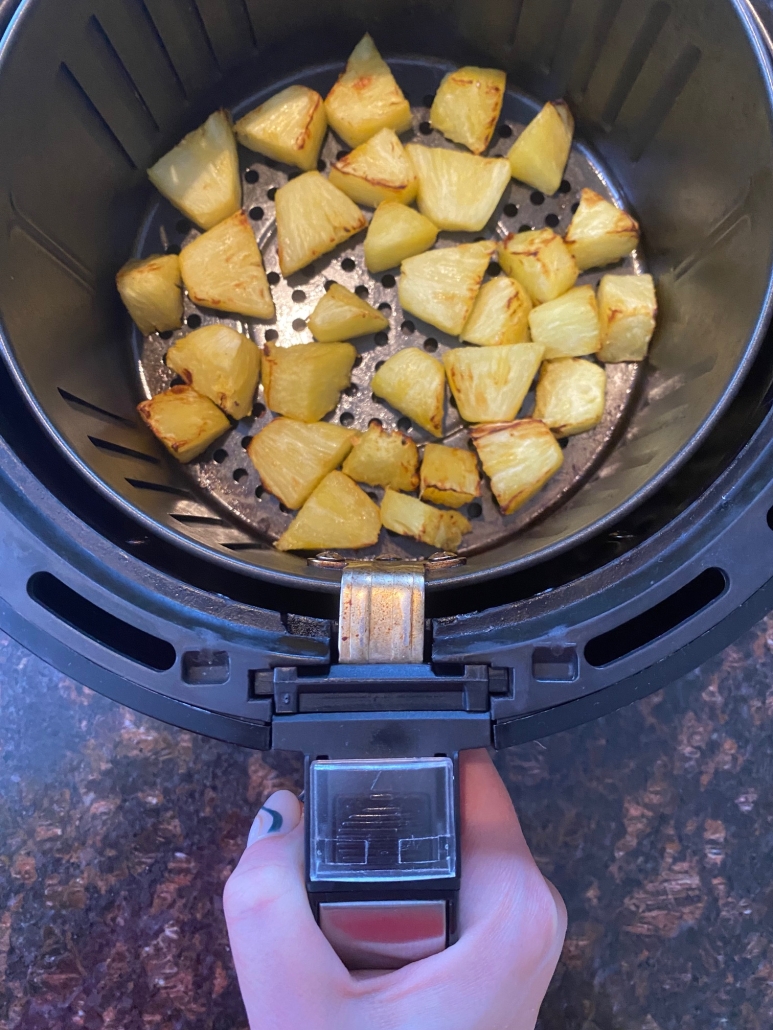 hand holding air fryer with pineapple chunks inside