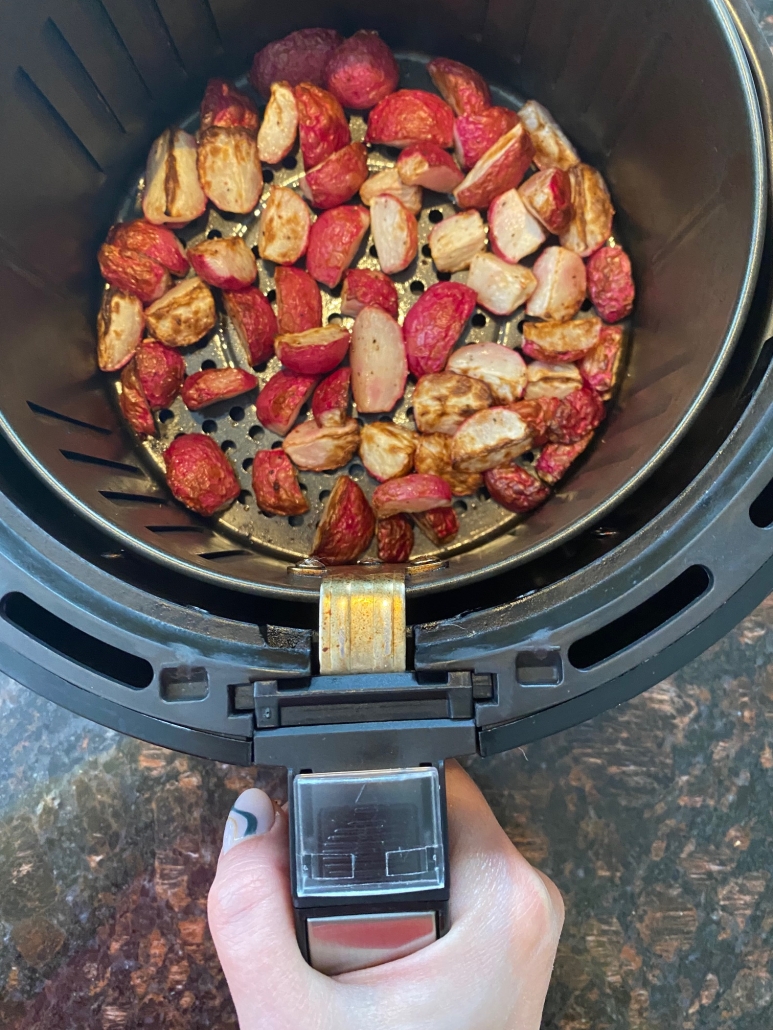 hand holding air fryer basket with sliced radishes inside