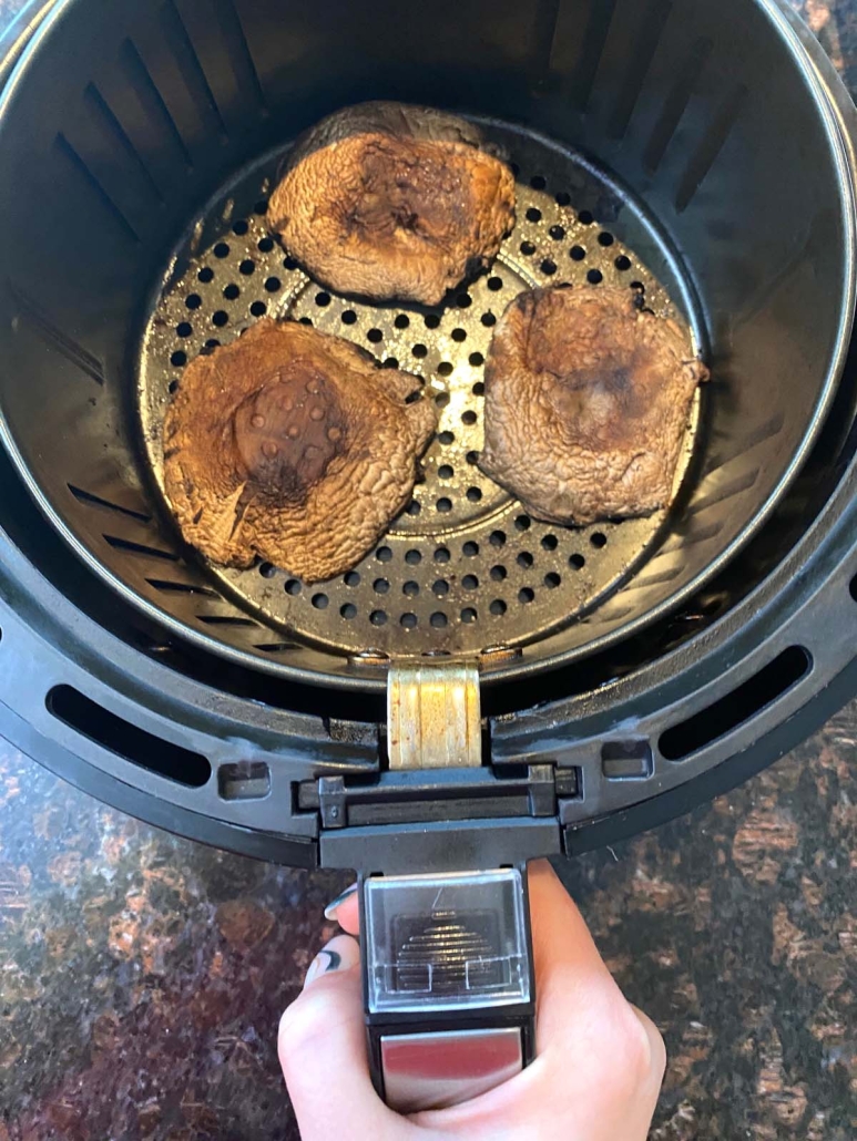 hand holding air fryer with portobello mushrooms