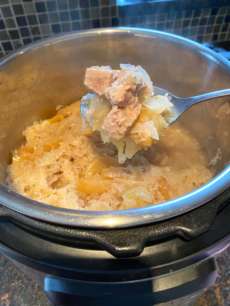 serving spoon holding cooked pork and sauerkraut in instant pot