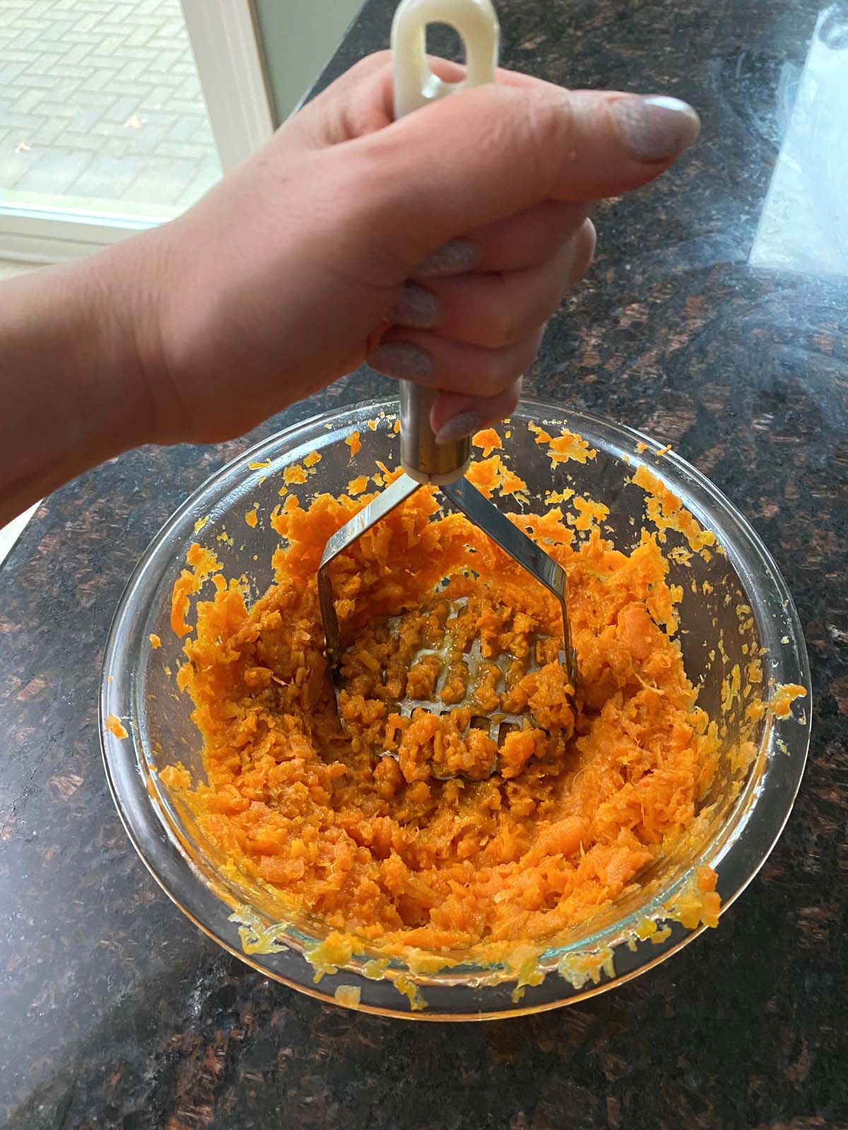 Cooked carrots being mashed with a potato masher.