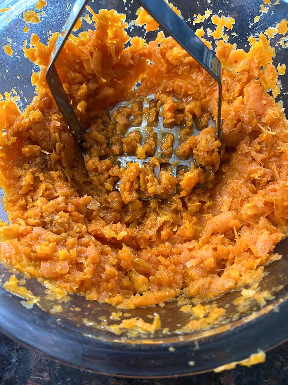 Cooked carrots being mashed with a potato masher.