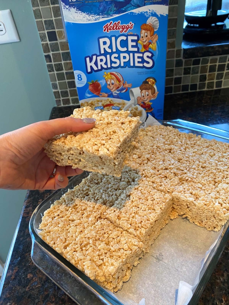 hand holding Microwave Rice Krispie Treat in front of pan of treats