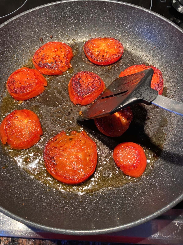 spatula flipping slices of seasoned tomato