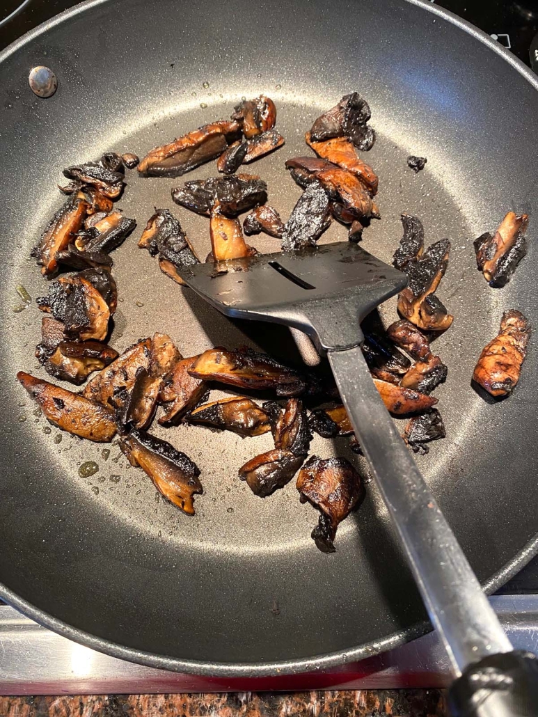 spatula stirring portobello mushrooms in a skillet