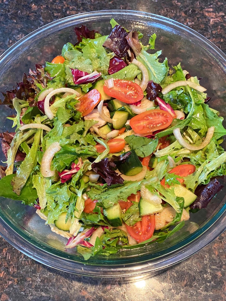 bowl of Spring Mix Salad topped with cucumbers, tomatoes, and onion