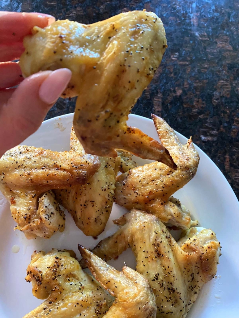 hand holding lemon pepper chicken wing baked in the oven