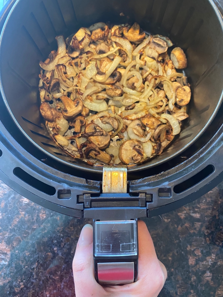 hand holding air fryer basket with cooked mushroom and onion slices inside