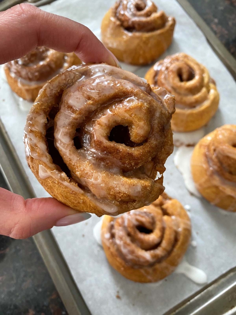 hand holding cinnamon roll over a tray of Crescent Roll Cinnamon Rolls