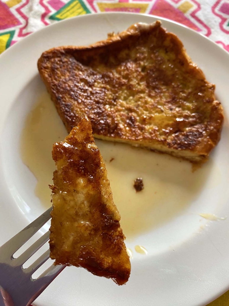 fork holding a piece of french toast with maple syrup drizzled on top