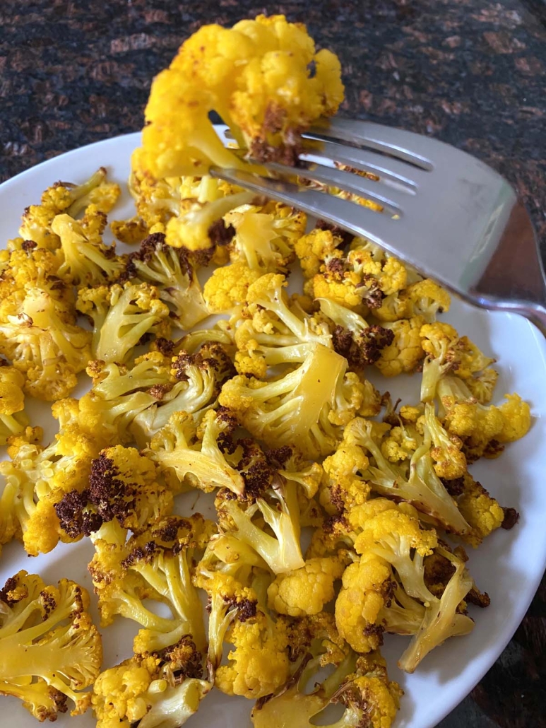 fork holding piece of golden brown orange cauliflower