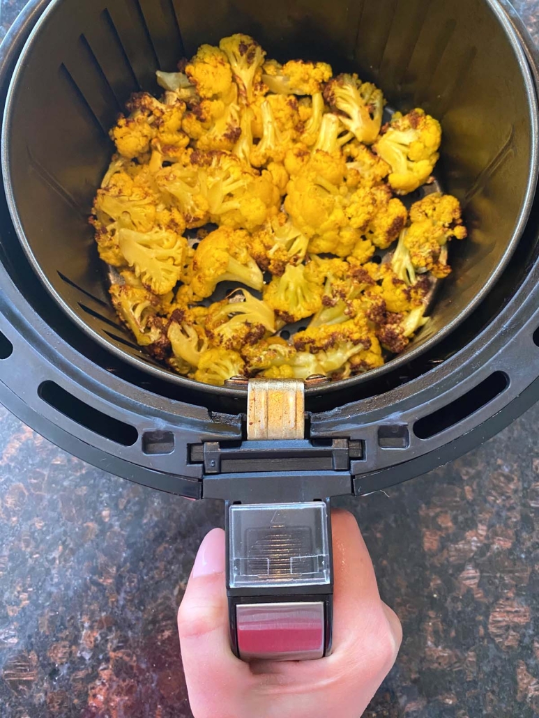 hand holding air fryer basket containing orange cauliflower
