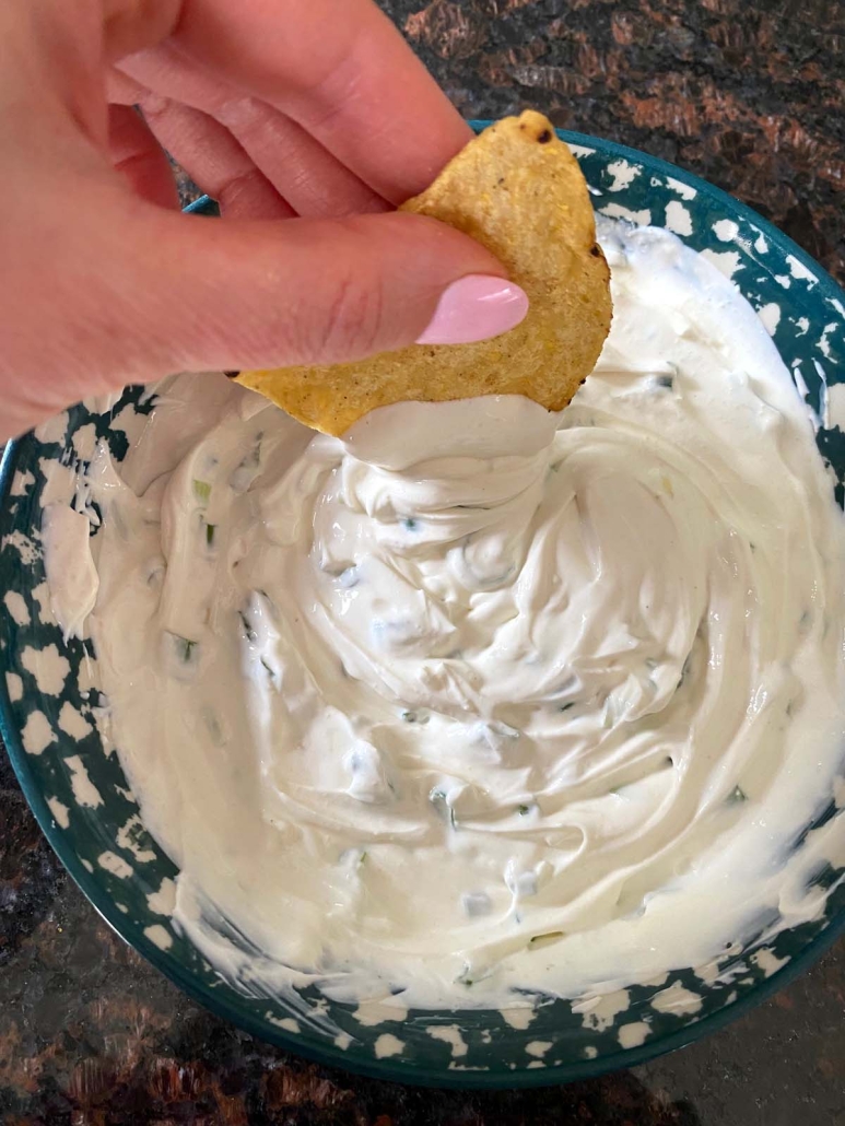 hand holding chip dipped in sour cream and onion dip