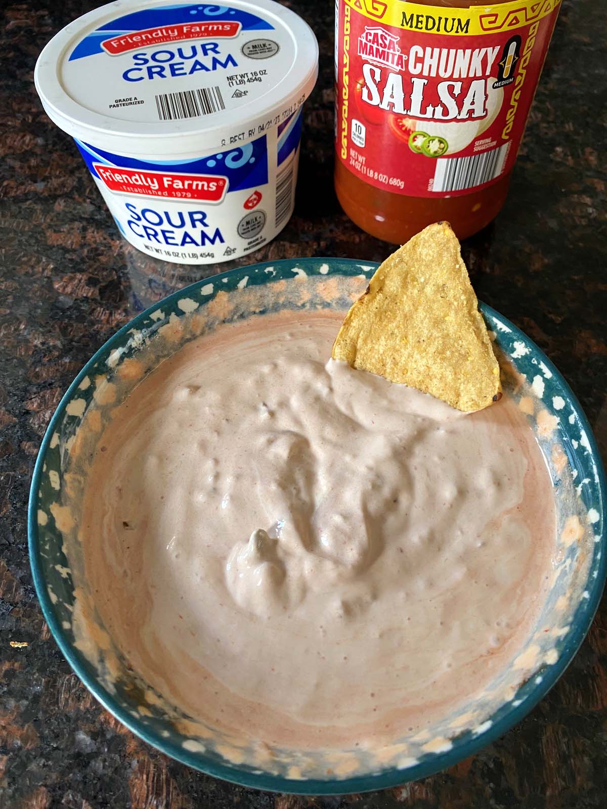 Bowl of sour cream and salsa dip with a container of sour cream and jar of salsa next to it. 