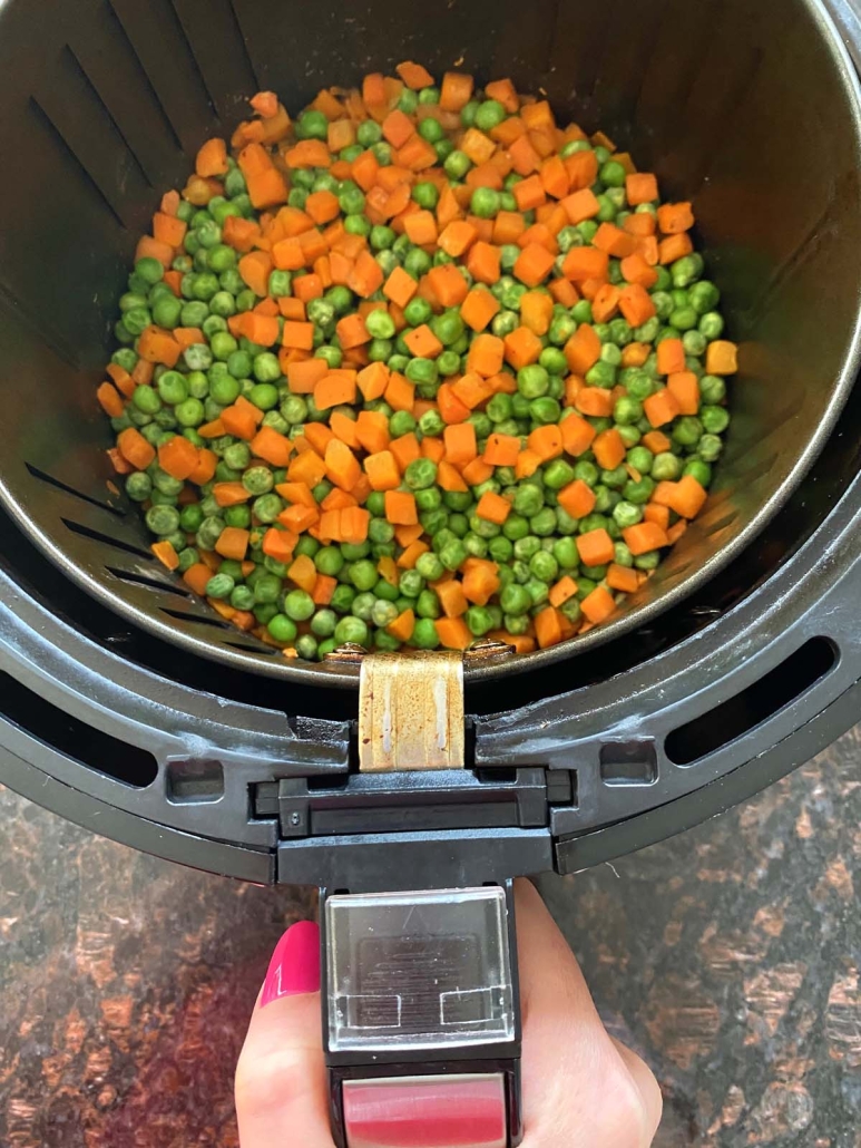 hand holding air fryer basket with peas and carrots inside