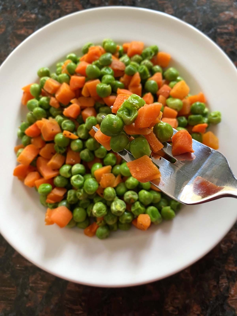 fork with a bite of air fryer cooked peas and carrots