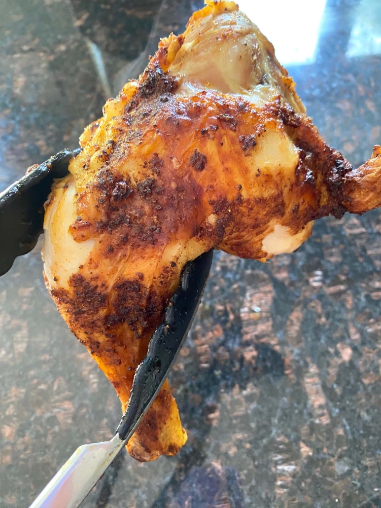tongs holding piece of Air Fryer Chicken Leg Quarter with crispy skin