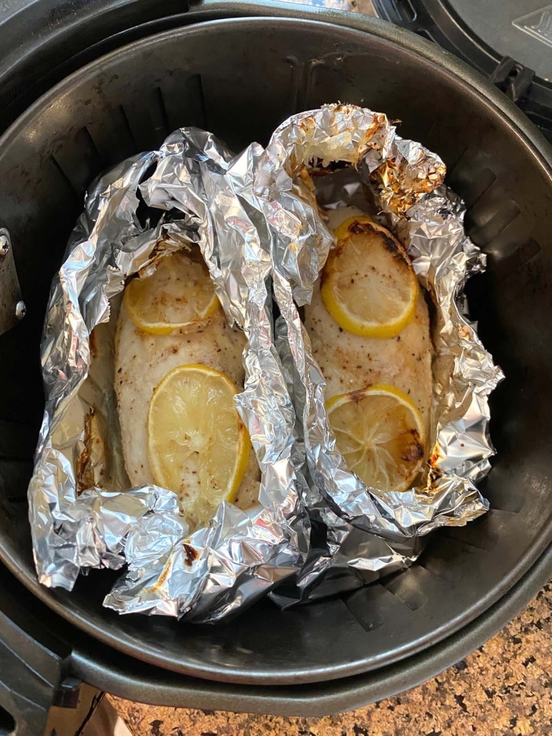air fryer basket with chicken breasts cooking in foil