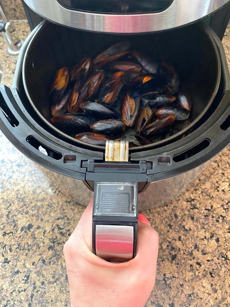 hand opening air fryer basket to show cooked mussels inside