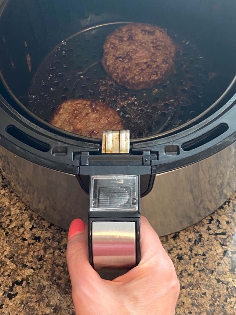 hand holding air fryer basket with Impossible burgers inside