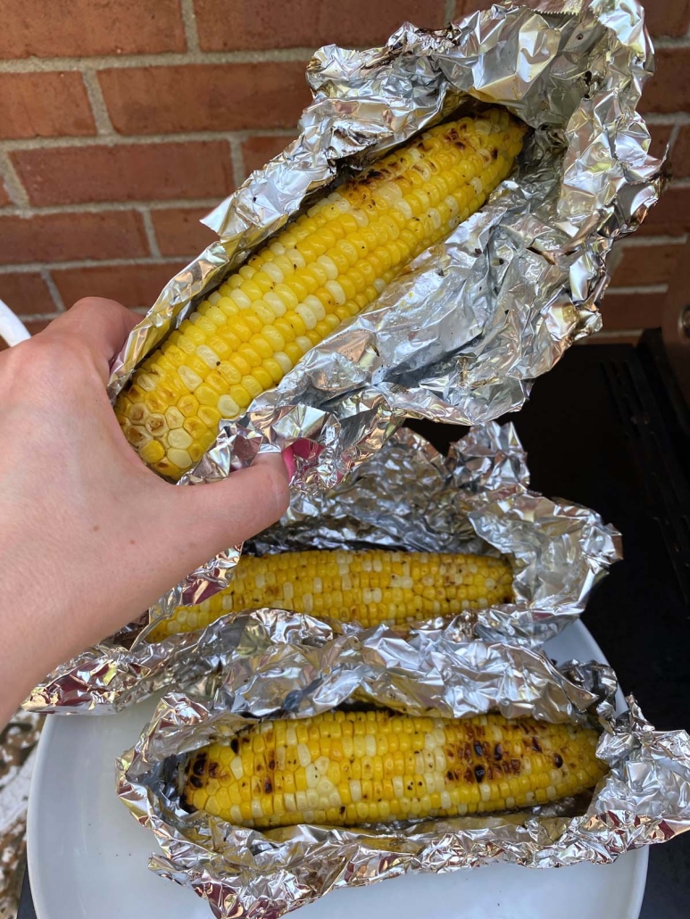 hand holding corn wrapped in foil