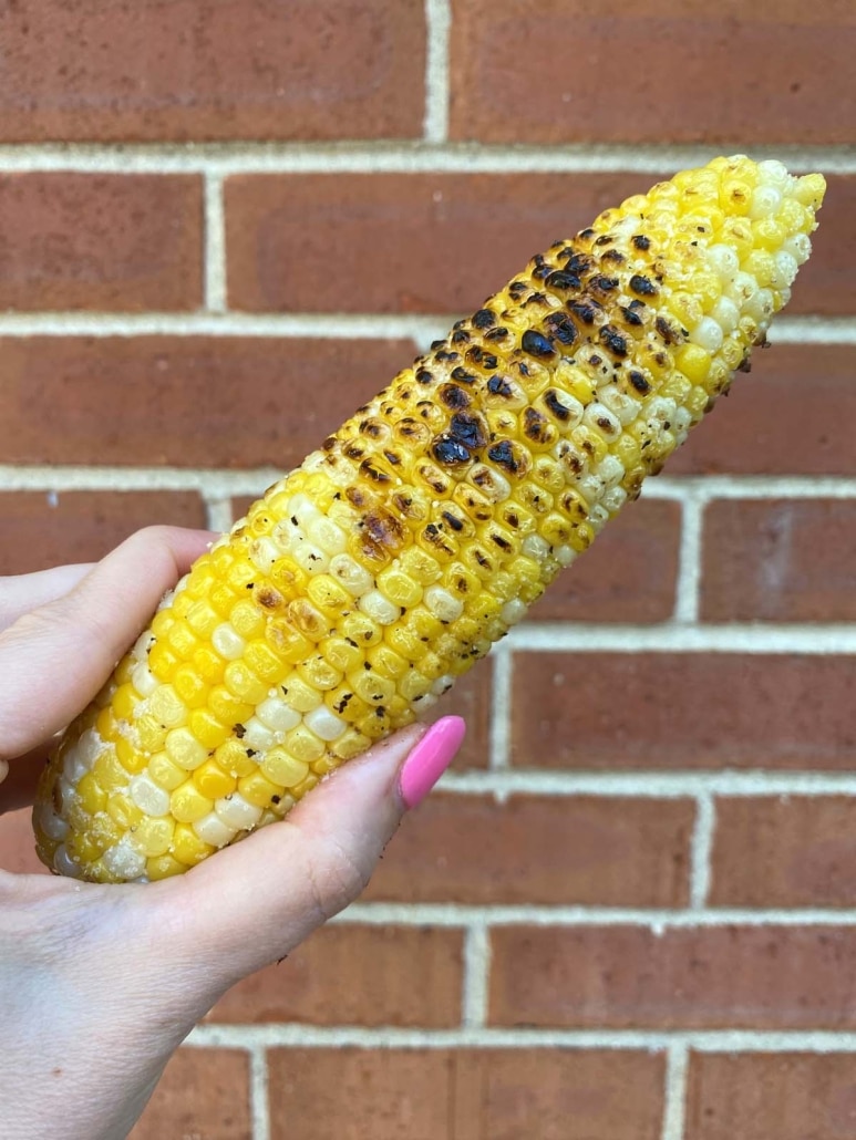 hand holding grilled corn on the cob (no husk)