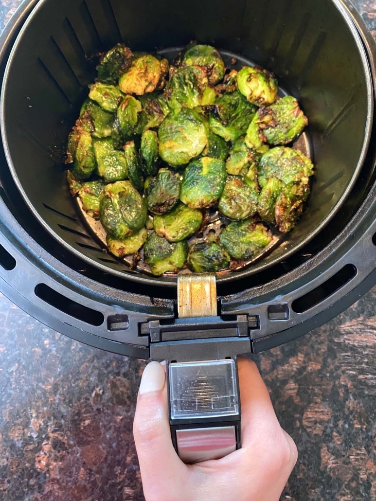 hand holding air fryer basket with Smashed Brussels Sprouts