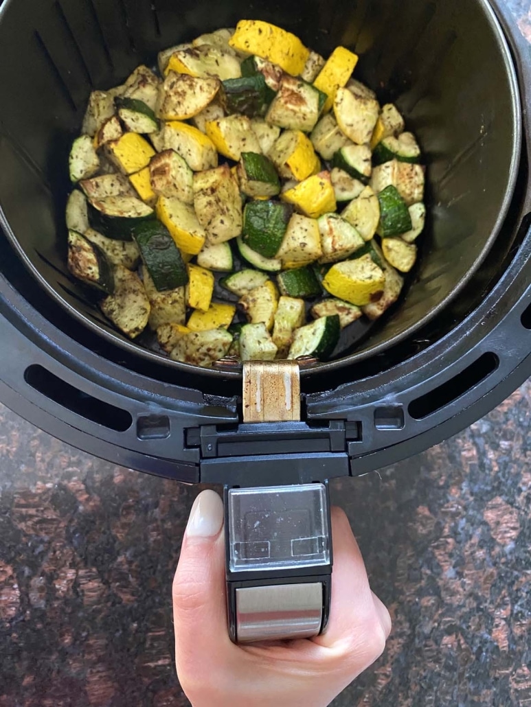 hand holding air fryer with chopped zucchini and squash inside