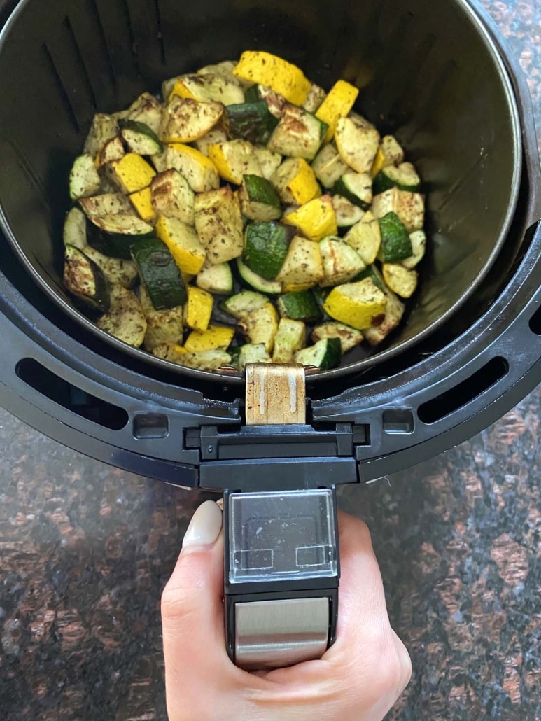 hand holding air fryer basket with Air Fryer Zucchini And Squash inside