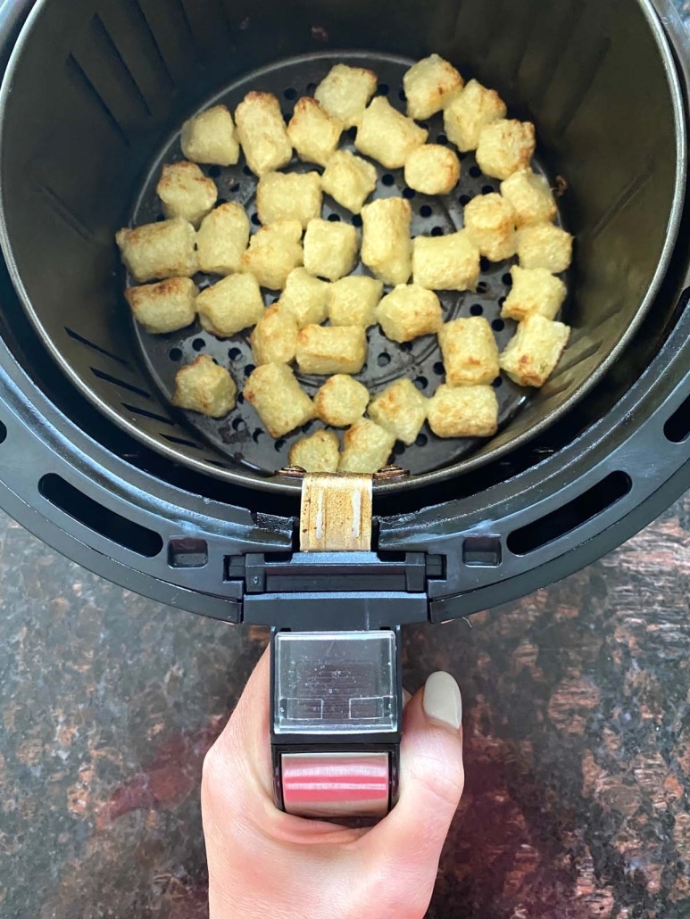 hand holding air fryer basket with low carb side dish cauliflower gnocchi inside