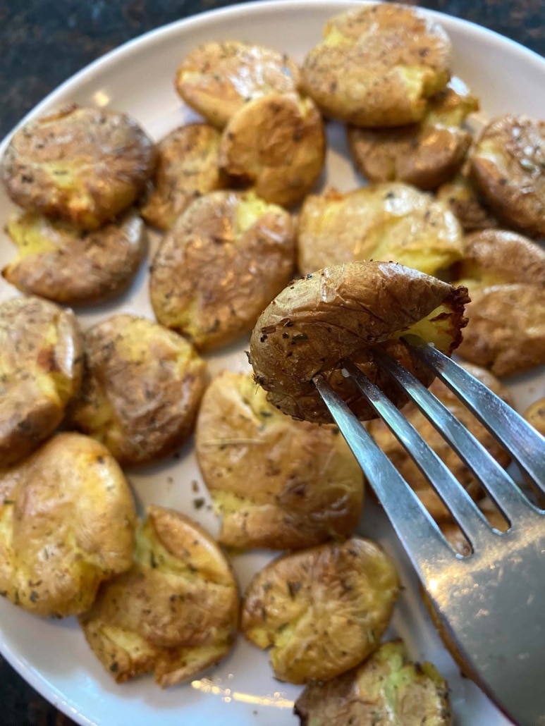 fork holding a golden brown, seasoned smashed potato