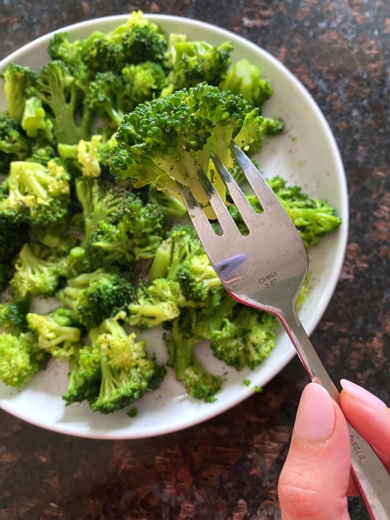 hand holding fork with boiled broccoli floret