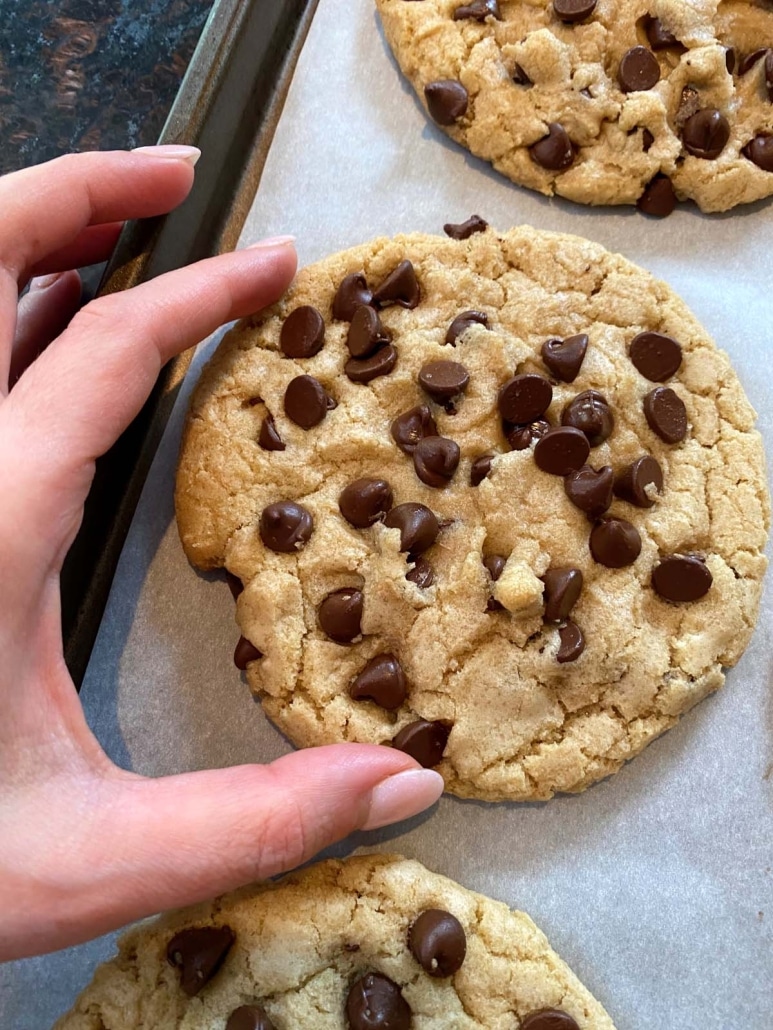 hand picking up Dairy Free Chocolate Chip Cookie from baking sheet