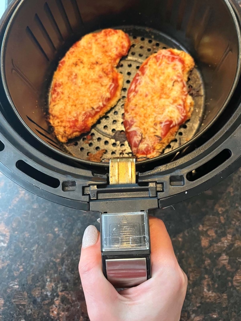 hand holding air fryer basket with Chicken Parmesan inside