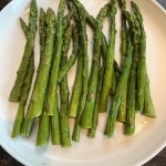 Top view of cooked frozen asparagus on a white plate placed over a stone sink.