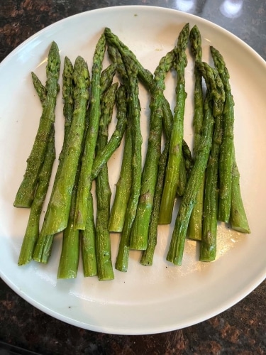 Top view of cooked frozen asparagus on a white plate placed over a stone sink.