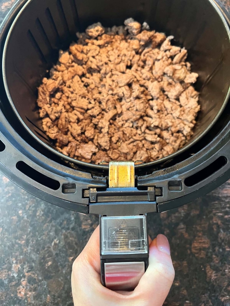 hand holding air fryer basket with seasoned ground turkey inside