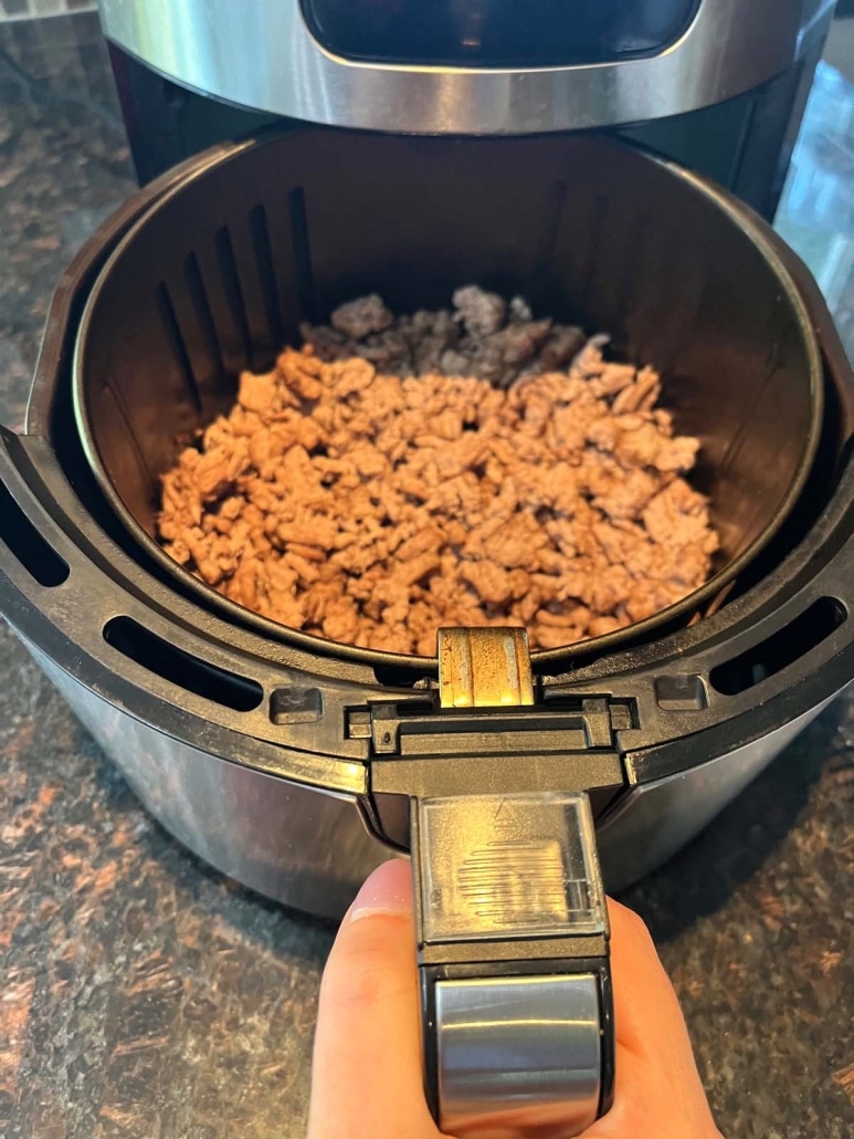 hand holding air fryer open to show cooked ground turkey inside