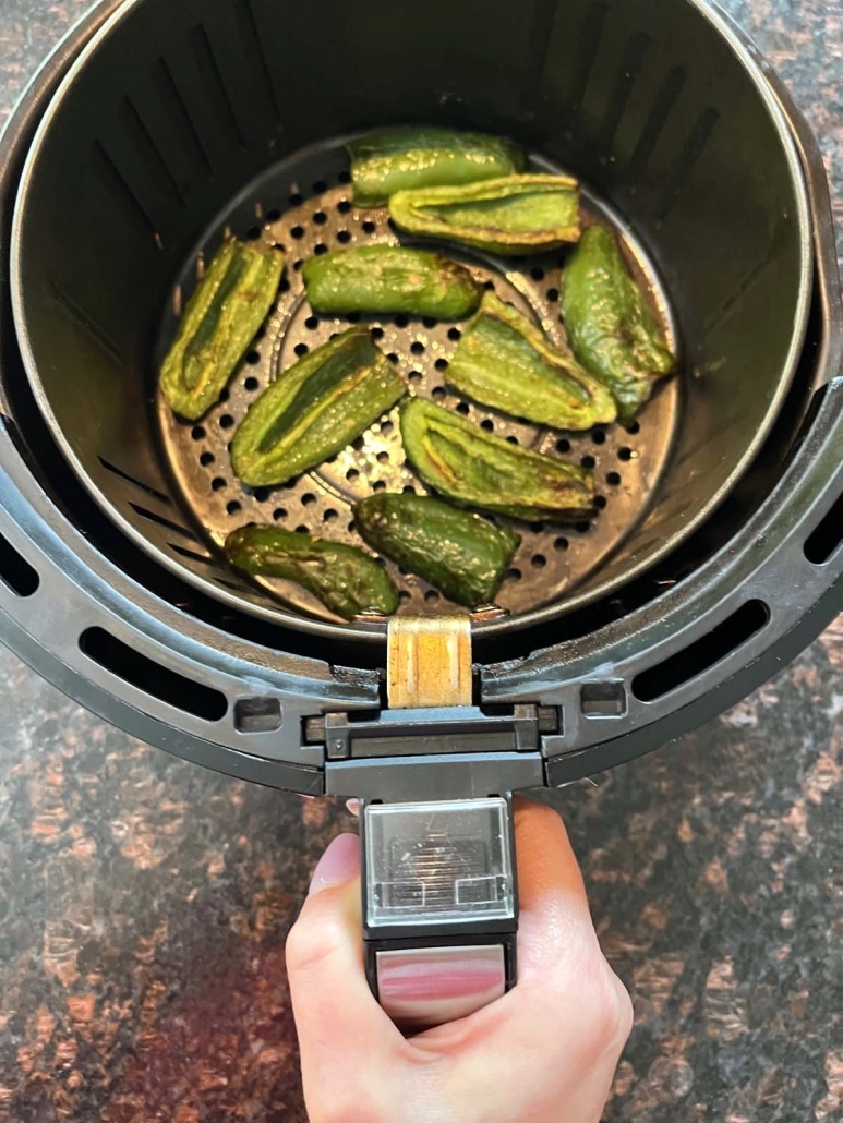 hand holding air fryer basket with Air Fryer Roasted Jalapeños inside